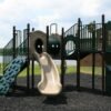 A playground with green slides, tube tunnels, climbing panels, mulch, grass, and a cloudy sky behind it.