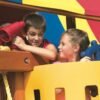 A pair of siblings standing under the shade of a Rainbow playset's colorful canopy and pretending to sail.