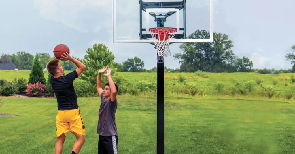 A pair of young teens playing basketball in front of a grassy area. One teen is preparing to make a shot in the basket.