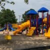 A colorful playground in a public play area, with several well-spaced slides, canopies, and unique play attractions.