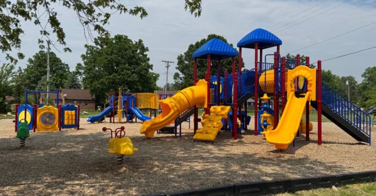 A colorful playground in a public play area, with several well-spaced slides, canopies, and unique play attractions.