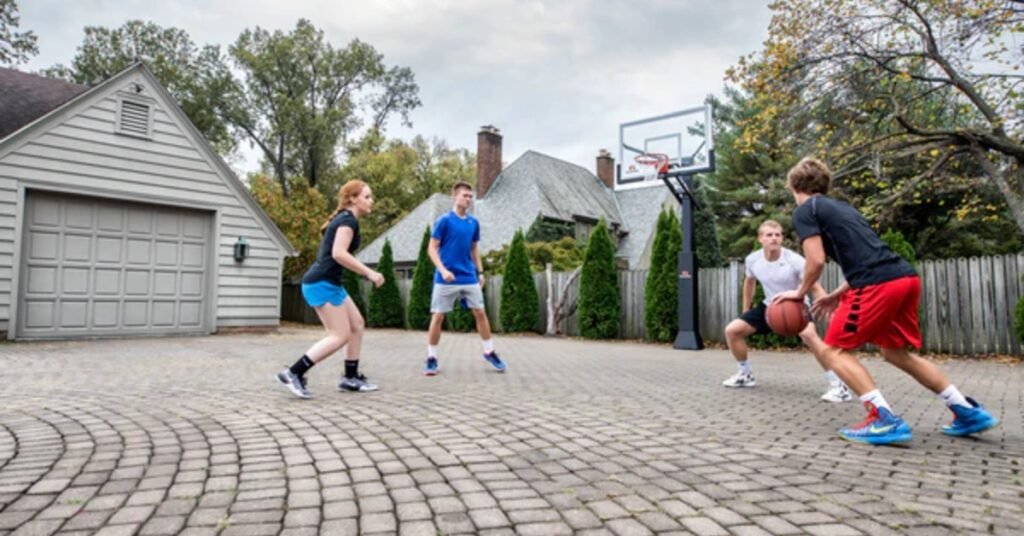A group of four kids playing basketball in the driveway in front of a garage. There is an in-ground basketball hoop.