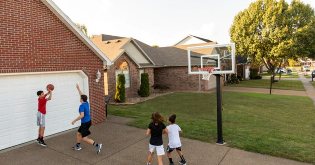 A group of four kids playing basketball in front of a garage on a large brick driveway with an in-ground hoop.