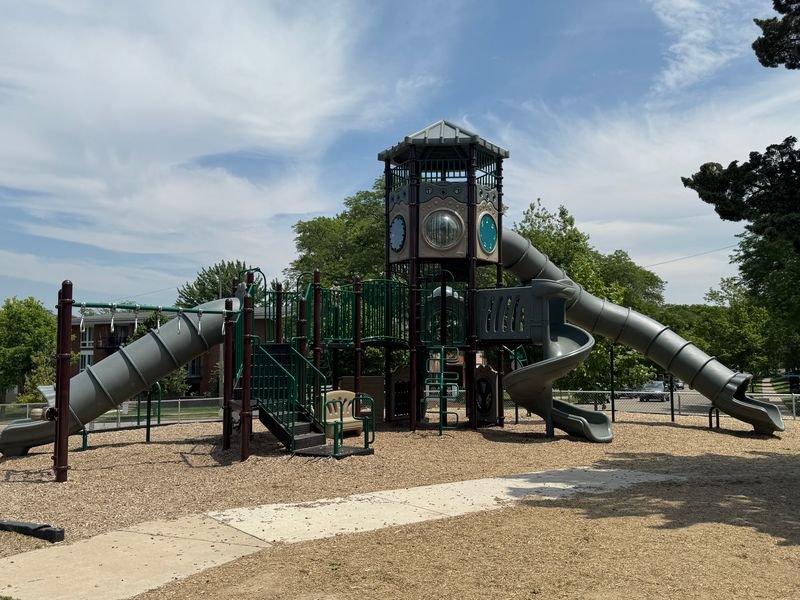 A large commercial playground with wide walkways and mulch around it. There are three large slides.