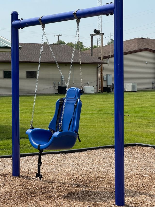 A blue swing on a sturdy structure. The swing is designed to be inclusive with a harness and larger seat bottom.