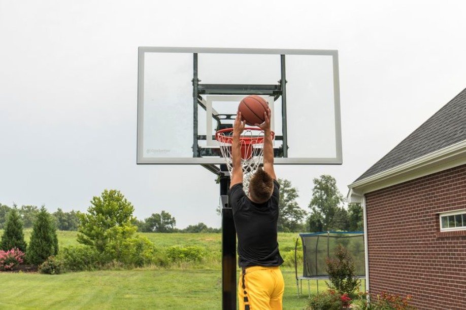 A young boy playing basketball at home. There's a brick structure to the right and he's trying to dunk the basketball.