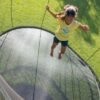 A young girl jumps on her Springfree trampoline at home. The sun is shining and she's dressed for summer.