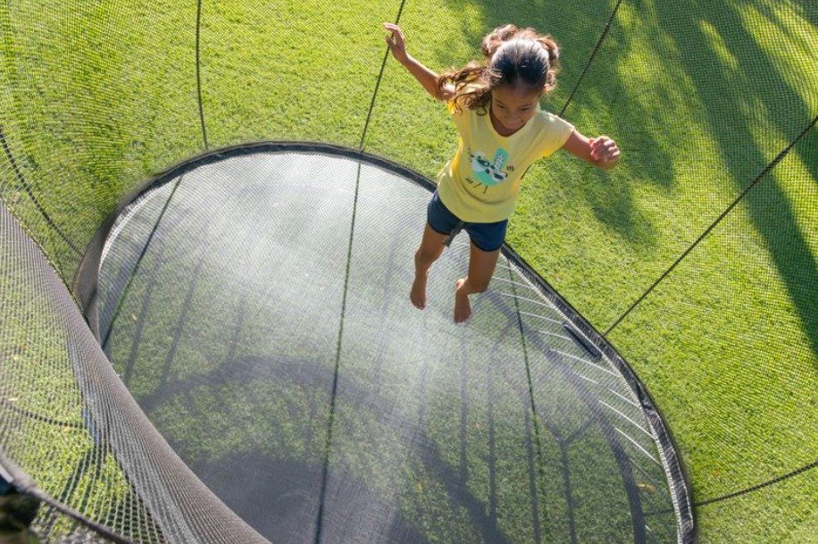 A young girl jumps on her Springfree trampoline at home. The sun is shining and she's dressed for summer.