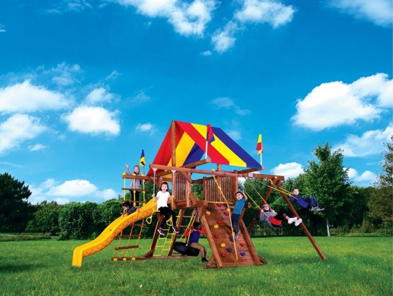 A beautiful sunny day with perfect blue skies overhead a playground set. There are kids swinging and climbing.