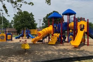 A colorful playground in a public play area, with several well-spaced slides, canopies, and unique play attractions.