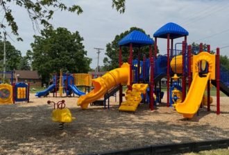 A colorful playground in a public play area, with several well-spaced slides, canopies, and unique play attractions.