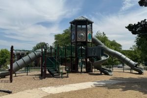 A large commercial playground with wide walkways and mulch around it. There are three large slides.
