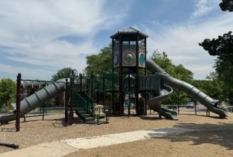 A large commercial playground with wide walkways and mulch around it. There are three large slides.